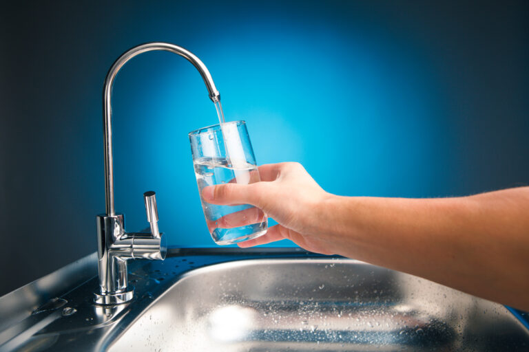hand pouring a glass of water from filter tap, blue background